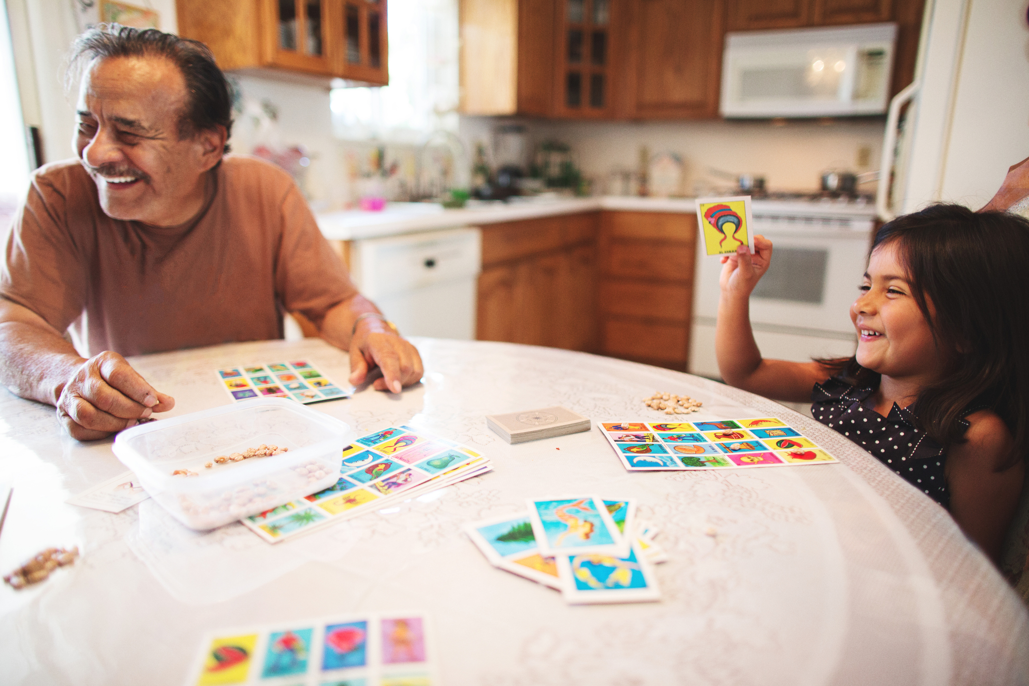 An image of a young girl playing a card game with her grandfather at the kitchen table.
